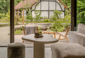 Uitzicht vanuit de woonkamer van Suite at Woodz Lodges, België, op het terras en een vakwerkhuis in de natuur.