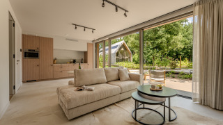 Moderne lodge-suite met open woonkamer, kitchenette en grote ramen met uitzicht op groene natuur.