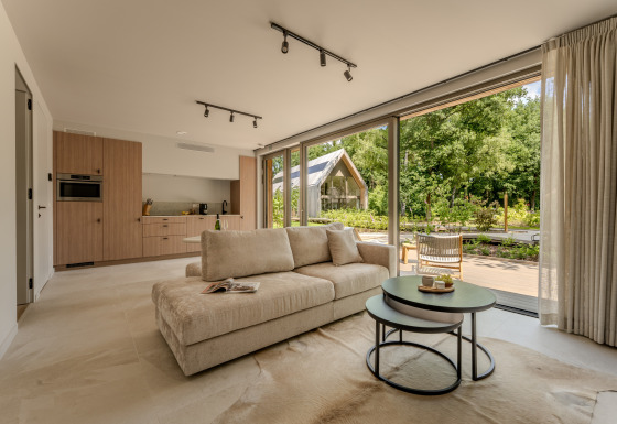 Moderne lodge-suite met open zithoek, kitchenette en grote ramen met zicht op het groen buiten.