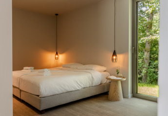 Dormitorio moderno en Suite de Woodz Lodges, Bélgica, con dos camas, lámparas colgantes y vista natural.