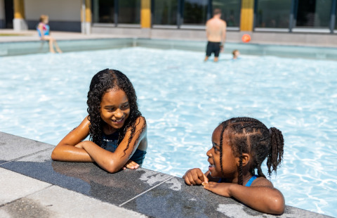 Dos niños sonríen y conversan juntos en una piscina del parque vacacional Hof van Salland en Overijssel, Países Bajos.