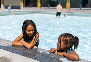 Zwei Kinder unterhalten sich lachend im Schwimmbad des Ferienparks Hof van Salland in Overijssel, Niederlande.