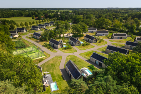 Luchtbeeld van een modern lodgepark met gezellige huisjes, privézwembaden en groene natuur rondom.
