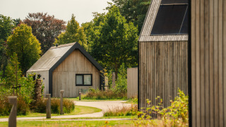 Moderne houten lodges in een rustige, groene omgeving met wandelpaadjes en omliggende bomen.