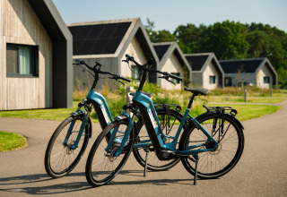Dos bicicletas eléctricas azules están aparcadas frente a modernas cabañas de madera con paneles solares.