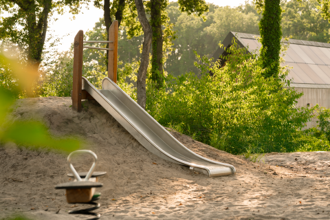Ein Spielplatz mit einer Metallrutsche und einem Wipptier bei einer Lodge in einem bewaldeten Gebiet.