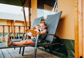 Girl relaxing on a lounge chair with tiger plush at waterfront luxury safari tent, Holiday Park Sallandshoeve.
