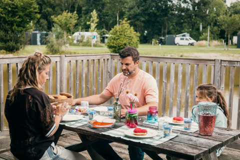 Gezin ontbijt aan een tafel buiten bij een luxe safaritent aan het water in Sallandshoeve.