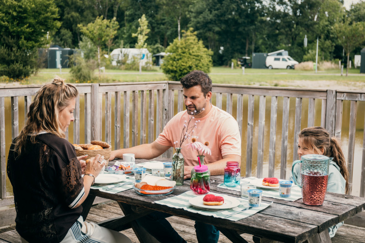 Familia disfruta del desayuno al aire libre junto a una tienda safari de lujo en la orilla en Sallandshoeve.