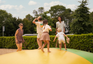 Familien spielen zusammen auf einem Outdoor-Luftkissen bei einer Lodge, umgeben von Natur und Grün.