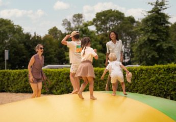 Familien spielen zusammen auf einem Outdoor-Luftkissen bei einer Lodge, umgeben von Natur und Grün.