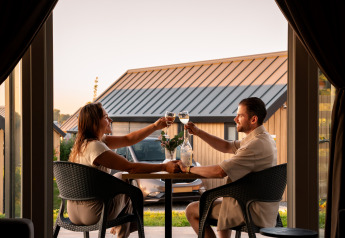 Couple toasting with wine at a romantic dinner in Berg Lodge - Sauna at Resort Mooi Bemelen, Netherlands.