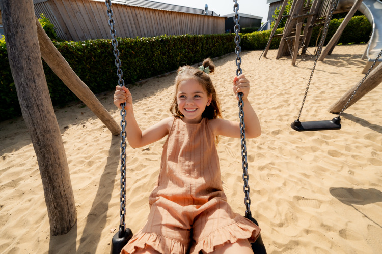 Girl swings on a sandy playground at a lodge, enjoying a sunny day in a joyful outdoor setting.