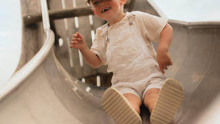 A young child in light overalls and a cap slides down a metal slide at Biebosch, Resort Mooi Bemelen in the Netherlands.