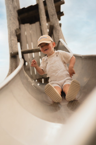 A young child in light overalls and a cap slides down a metal slide at Biebosch, Resort Mooi Bemelen in the Netherlands.