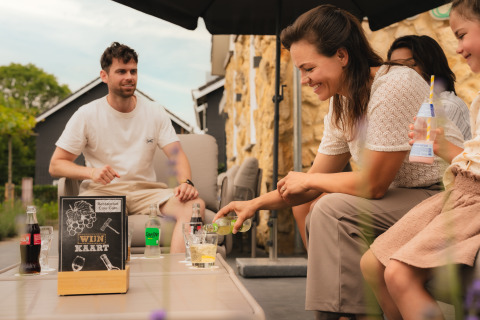 Una familia sonriente disfruta de bebidas al aire libre en un lodge, con carteles y bebidas sobre la mesa.