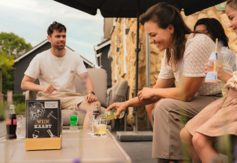 Una familia sonriente disfruta de bebidas al aire libre en un lodge, con carteles y bebidas sobre la mesa.