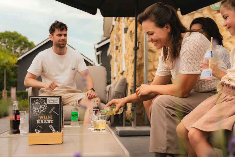 A smiling family enjoys drinks together outdoors at a lodge, with signs and beverages on the table.