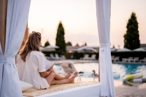 Mujer leyendo junto a la piscina en Biebosch, Resort Mooi Bemelen, Países Bajos, al atardecer.