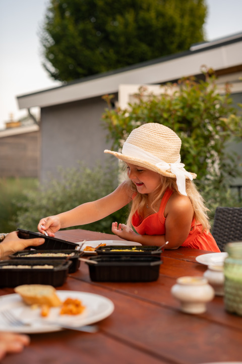 Una niña con sombrero disfruta de una comida al aire libre en Lodge Biebosch, Resort Mooi Bemelen, Países Bajos.