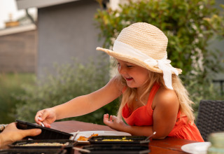 Una niña con sombrero disfruta de una comida al aire libre en Lodge Biebosch, Resort Mooi Bemelen, Países Bajos.