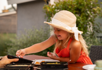 A young girl wearing a hat eats outdoors at a table at Lodge Biebosch, Resort Mooi Bemelen, Netherlands.