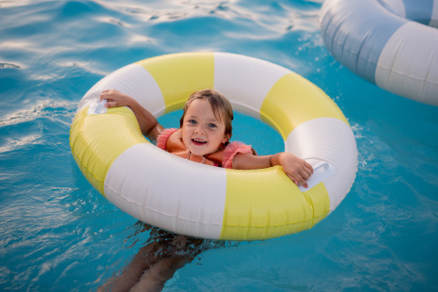 Un enfant sourit dans une bouée jaune et blanche à la piscine du Biebosch Lodge, Resort Mooi Bemelen, Pays-Bas.
