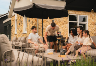 Fünf Personen, darunter ein Kind, entspannen sich auf der Terrasse einer gemütlichen Lodge mit Steinwand.