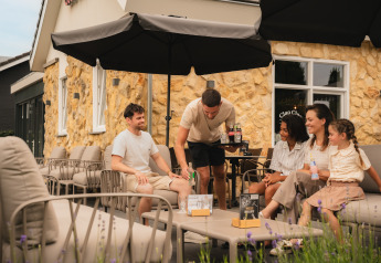 Fünf Personen, darunter ein Kind, entspannen sich auf der Terrasse einer gemütlichen Lodge mit Steinwand.