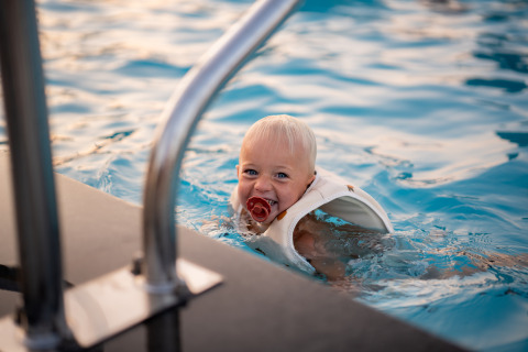 Un niño pequeño con chupete y chaleco salvavidas disfruta nadando en la piscina de Biebosch, Resort Mooi Bemelen.