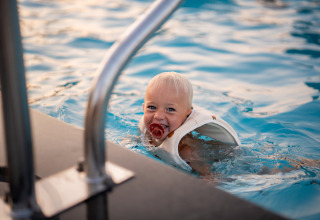 Un niño pequeño con chupete y chaleco salvavidas disfruta nadando en la piscina de Biebosch, Resort Mooi Bemelen.