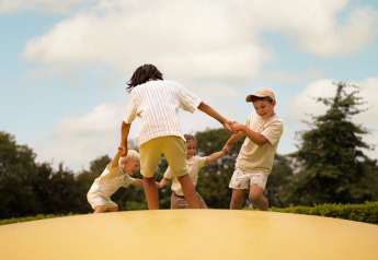 Children playing together outside on a bouncy platform at Lodge Biebosch, Resort Mooi Bemelen, Netherlands.