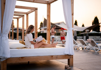 Woman reading a book on a canopy daybed by the pool at Biebosch Lodge, Resort Mooi Bemelen, Netherlands.