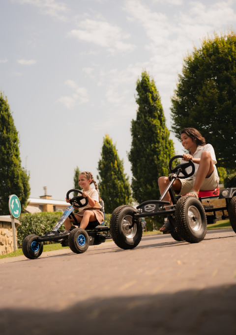 Twee kinderen rijden op skelters en lachen buiten bij Biebosch - tuinhuis op Resort Mooi Bemelen, Nederland.