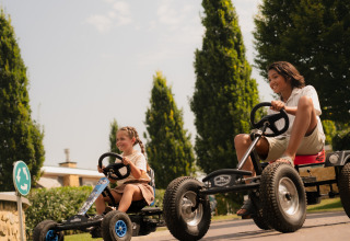 Zwei Kinder fahren Gokarts und lachen draußen bei Biebosch - tuinhuis im Resort Mooi Bemelen, Niederlande.