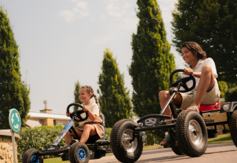 To børn kører gokarts og smiler udendørs ved Biebosch - tuinhuis på Resort Mooi Bemelen, Holland.