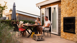 Eine Familie isst gemeinsam im Freien auf der Terrasse einer gemütlichen Lodge bei Sonnenuntergang.