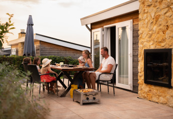 Una familia disfruta de una cena al aire libre en la terraza de una acogedora cabaña al atardecer.