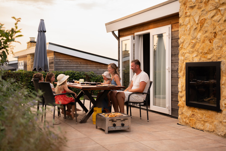 Una familia disfruta de una cena al aire libre en la terraza de una acogedora cabaña al atardecer.