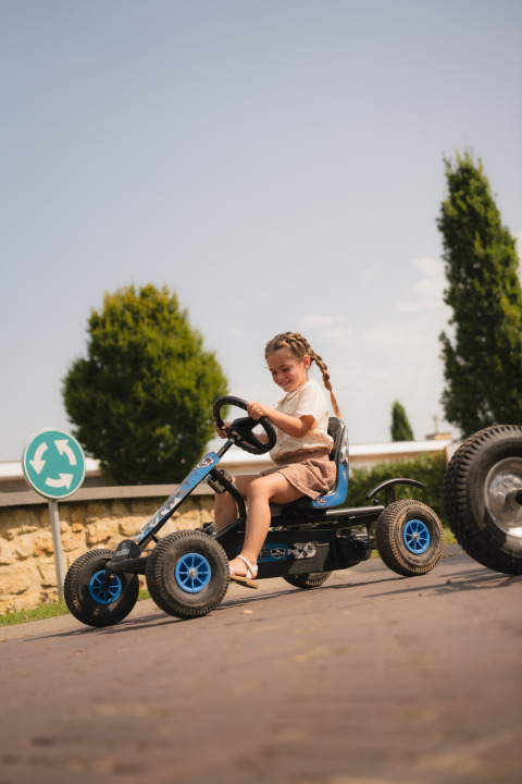 Una niña conduce un kart de pedales en Biebosch - Sunshower, Resort Mooi Bemelen, Países Bajos, en verano.