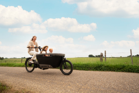 Famiglia felice in bicicletta cargo sulla strada presso Biebosch - Sunshower, Resort Mooi Bemelen, Paesi Bassi.