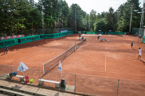 Clay tennis courts at Camping GT Keiheuvel holiday park in Antwerp, Belgium, surrounded by lush trees.