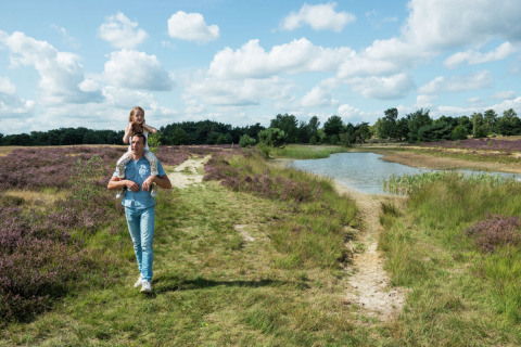 Father carrying daughter on shoulders on a trail by a pond at Camping GT Keiheuvel, Antwerp, Belgium.