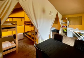 Interior de una tienda safari en Camping GT Keiheuvel, Bélgica, con literas, mesa y zona de cocina.