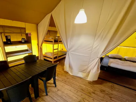 Intérieur d'une tente safari avec lits superposés, lit double et table à manger au Camping GT Keiheuvel, Belgique.