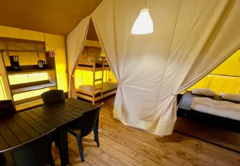 Innenraum eines Safarizelts mit Etagenbett, Doppelbett und Esstisch auf Camping GT Keiheuvel, Belgien.