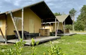 Tiendas safari en Camping GT Keiheuvel en Bélgica, con terrazas elevadas y muebles de exterior en zonas verdes.