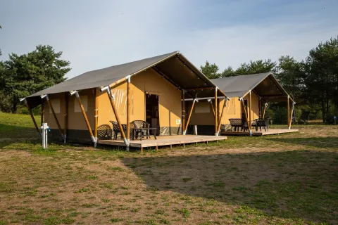 Zwei moderne Safarizelte mit Veranda und Gartenmöbeln auf einem Campingplatz umgeben von Bäumen.
