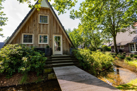 Charmant houten A-frame vakantiehuis in Hof van Salland, Overijssel, omgeven door groen en water.