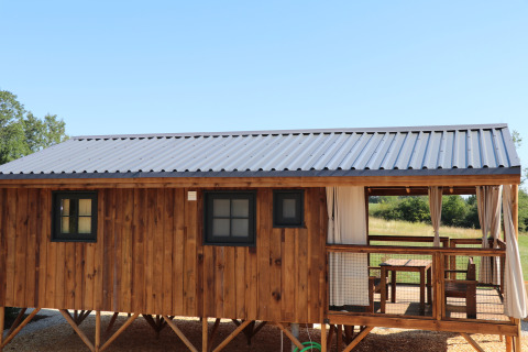 Holz-Lodge mit Metall-Dach und gemütlicher Veranda, umgeben von Natur, sonniger Tag im Freien.